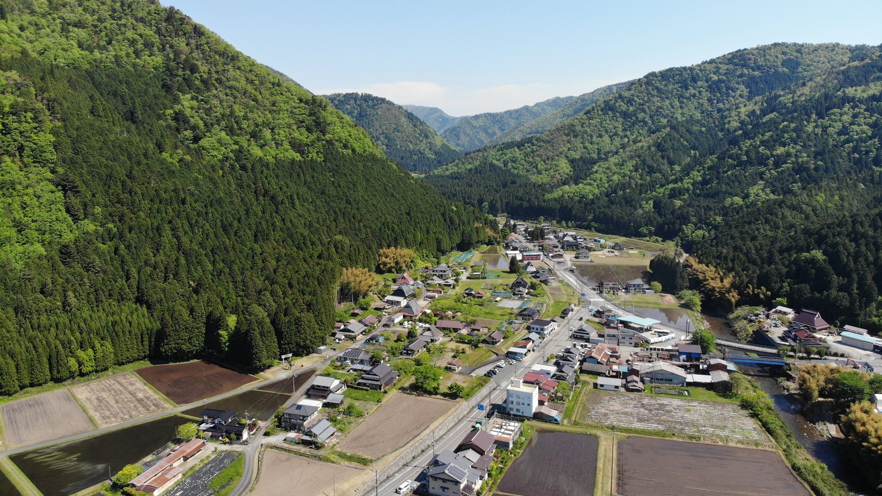 山に囲まれた美山の集落を上空から見たところ。谷筋に沿って家々と田んぼが並び、右手に川が流れている